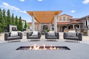 A fire pit in the middle of a patio with chairs around it